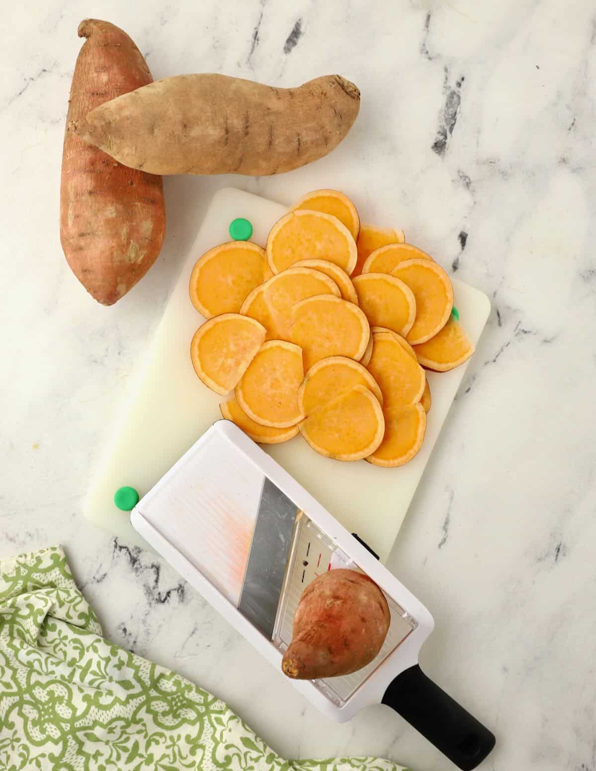 A mandoline and sliced sweet potatoes on a cutting board.  