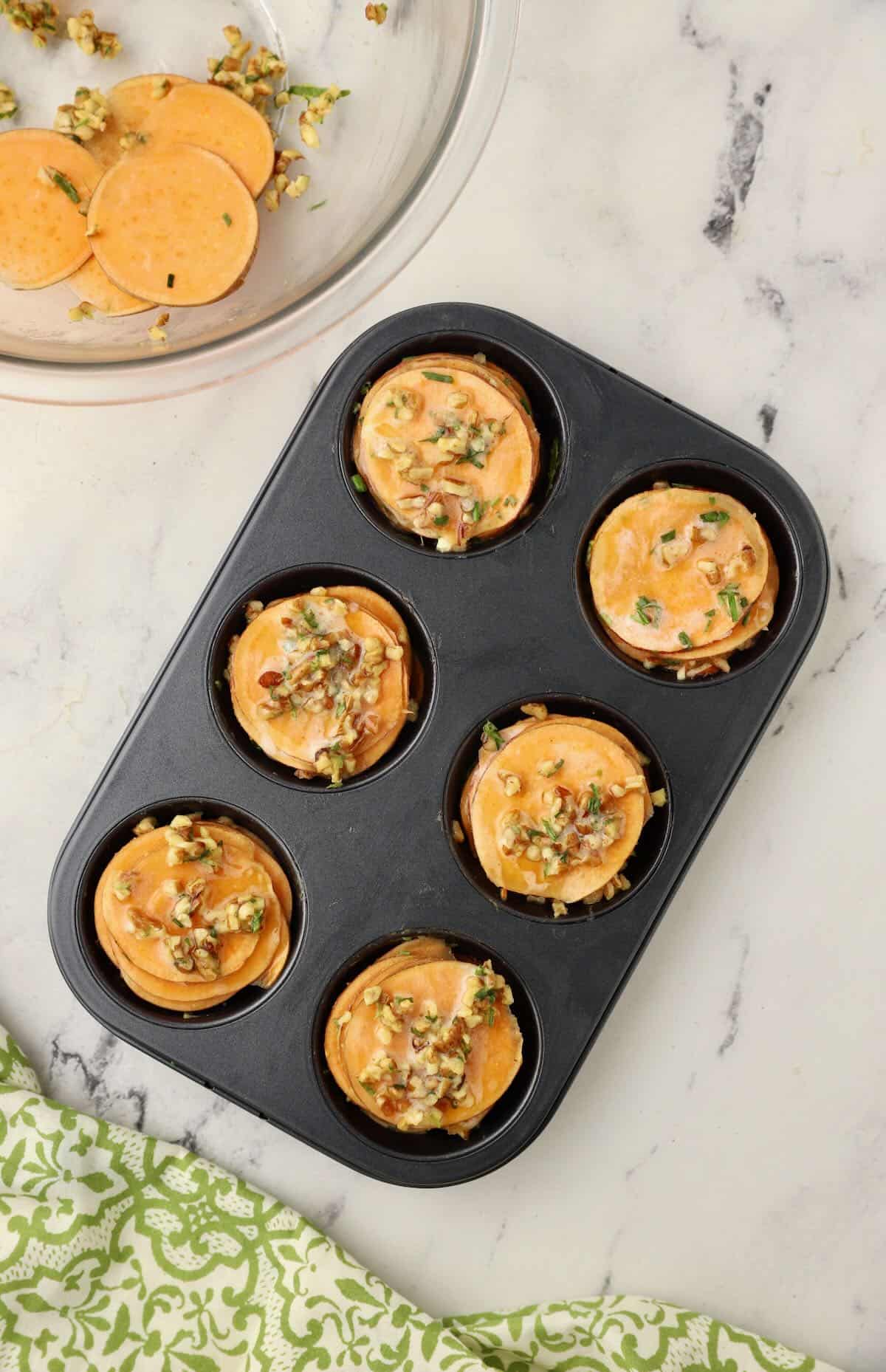 A muffin pan full of thinly sliced sweet potatoes. 