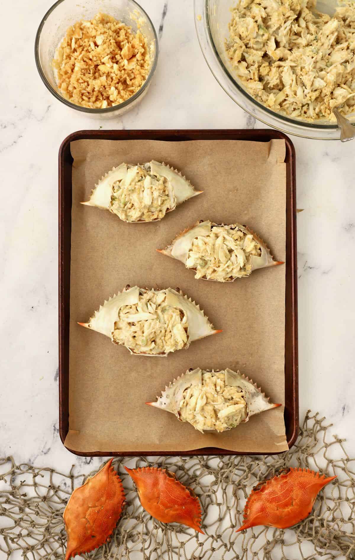 Blue crab shells stuffed with deviled crab mixture on a baking sheet. 