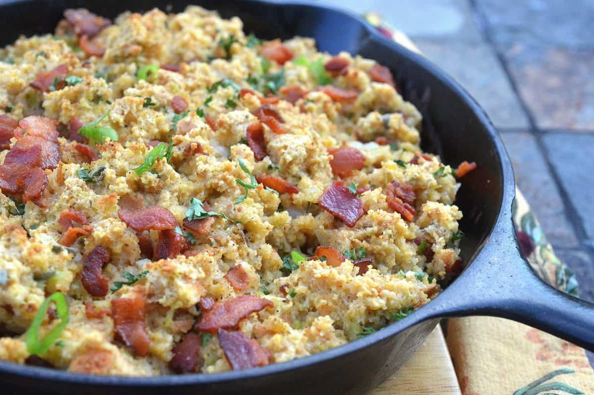 A cast iron skillet full of cornbread stuffing topped with crumbled bacon. 