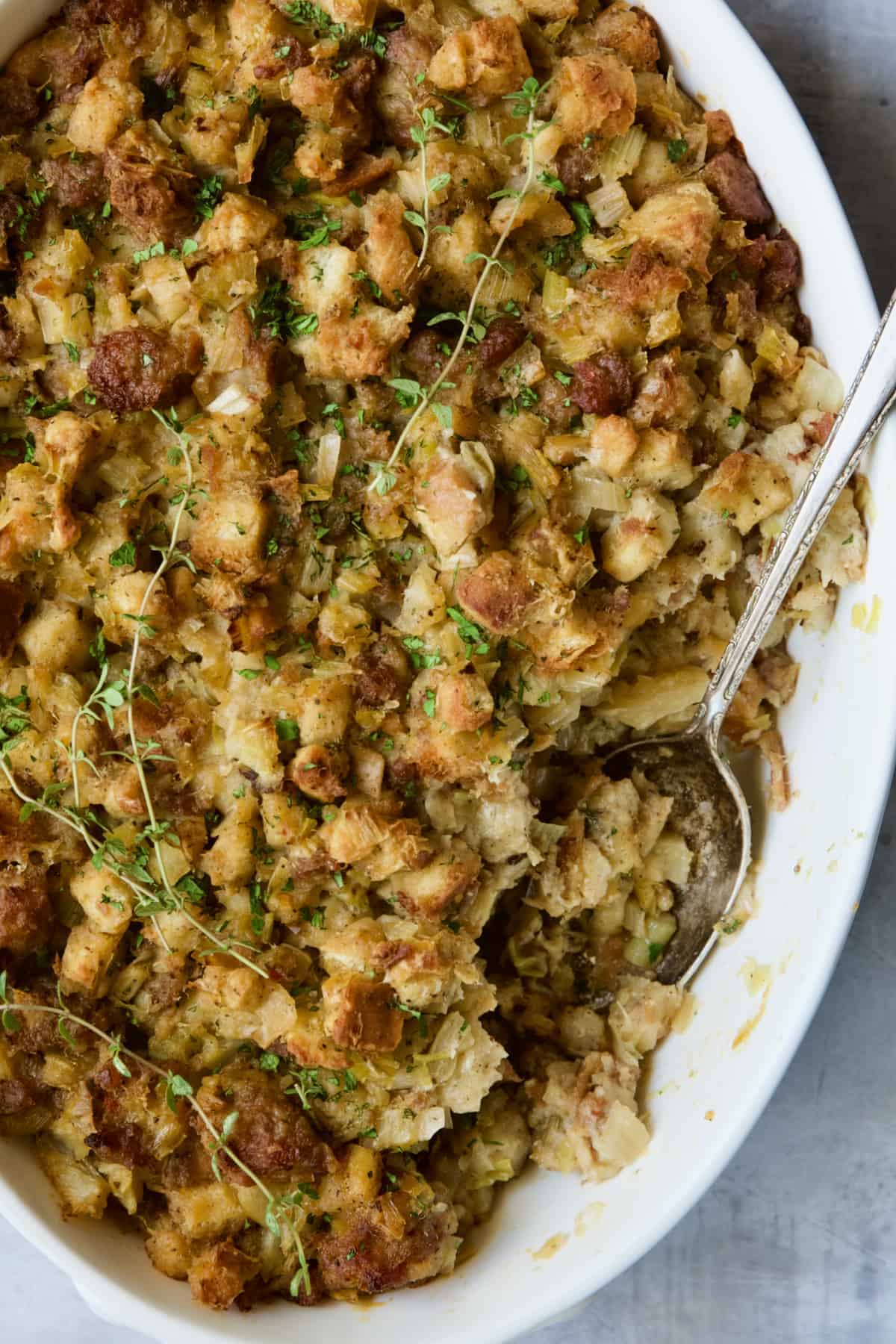 A white casserole dish full of stuffing garnished with thyme sprigs. 
