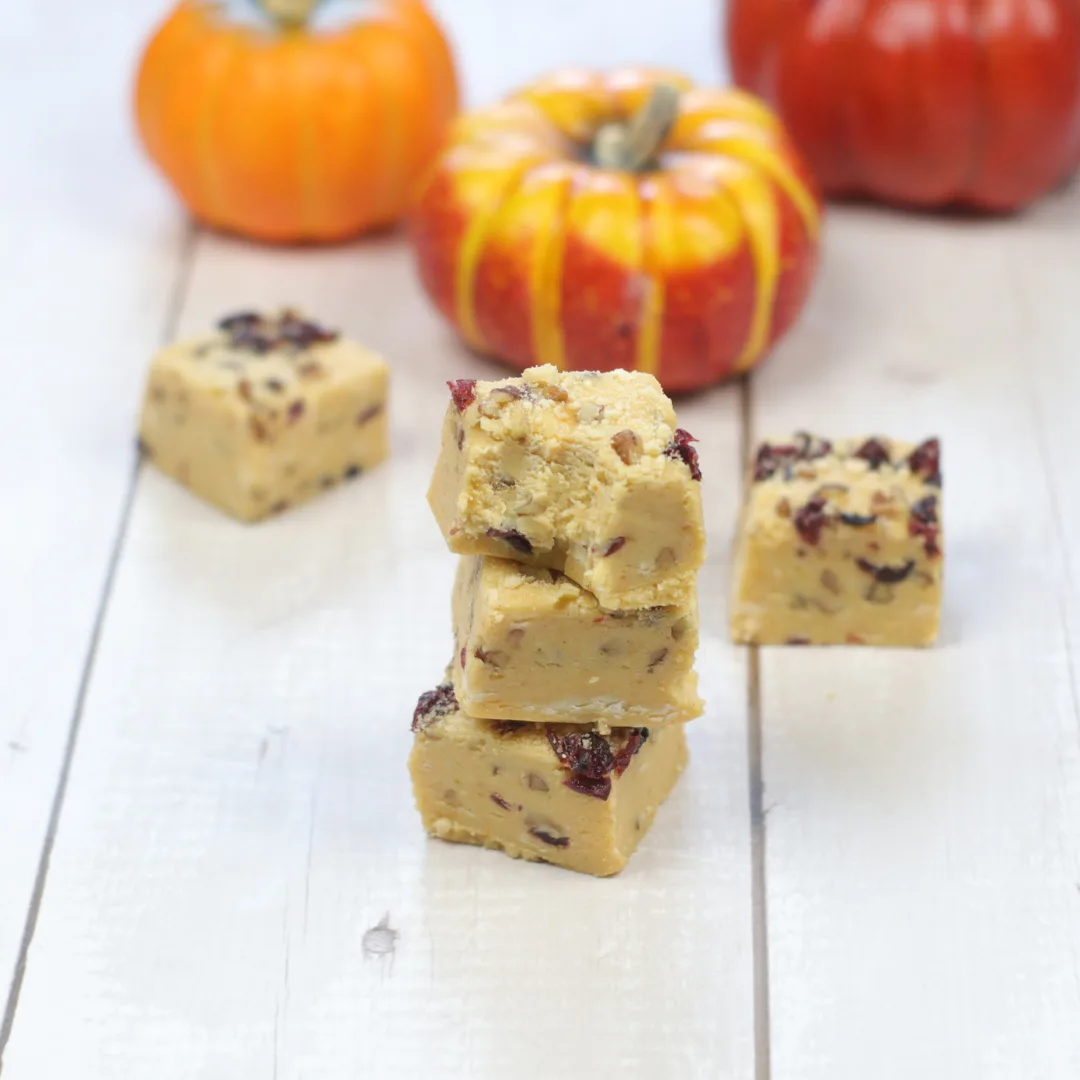 Thanksgiving fudge stacked on a white board with pumpkins in the background. 