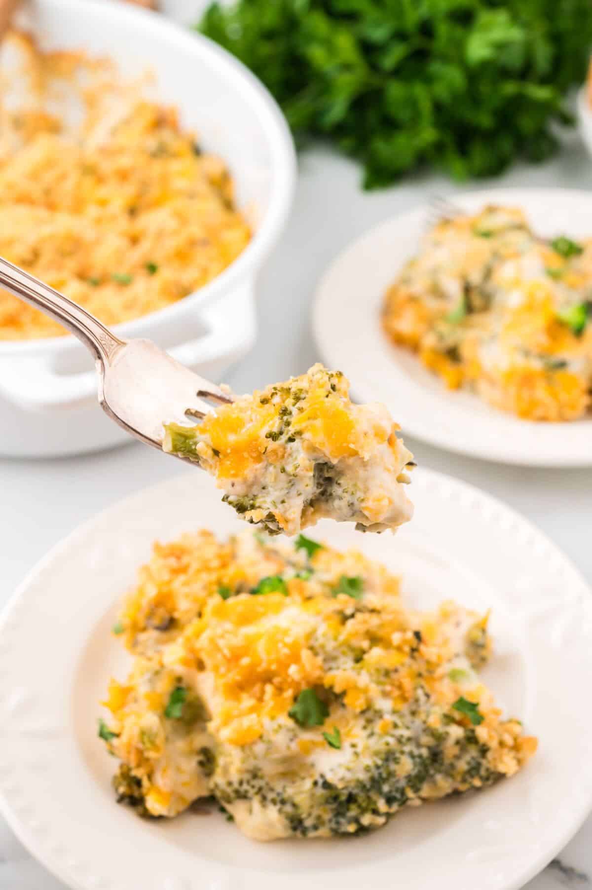 A serving of broccoli cheese casserole topped with crushed Ritz crackers on a white plate with a forkful above it. 