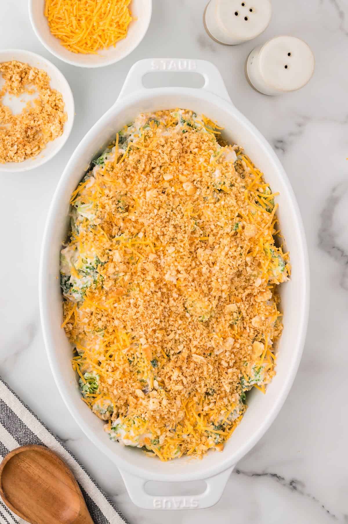 Broccoli cheese casserole topped with crushed Ritz crackers in an oval baking dish ready to bake. 