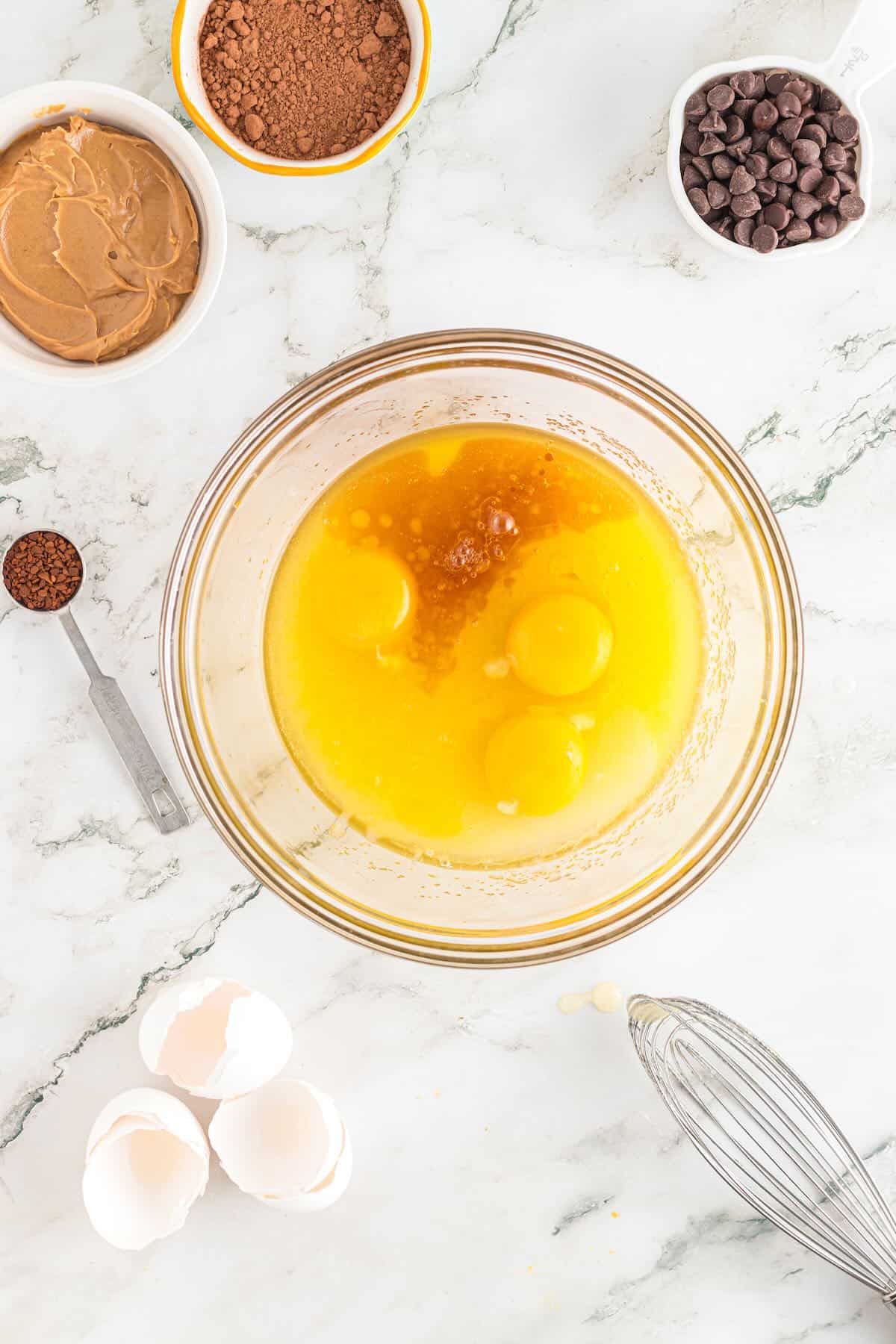 Clear glass bowl with melted butter, sugar, eggs, and vanilla extract. 
