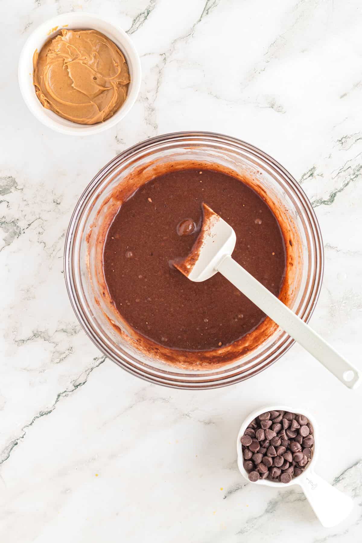 Brownie batter in a clear glass bowl with a spatula. 