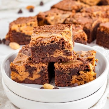 Three chocolate peanut butter brownies stacked on a white plate.