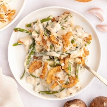 A serving of green bean casserole on a white plate with a spoon.