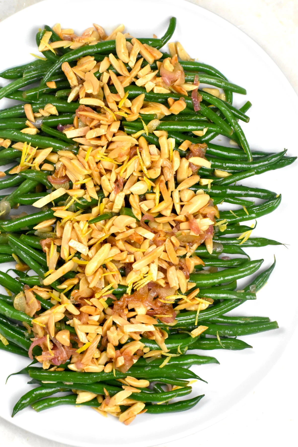 Green beans almondine on a white plate topped with sliced almonds. 
