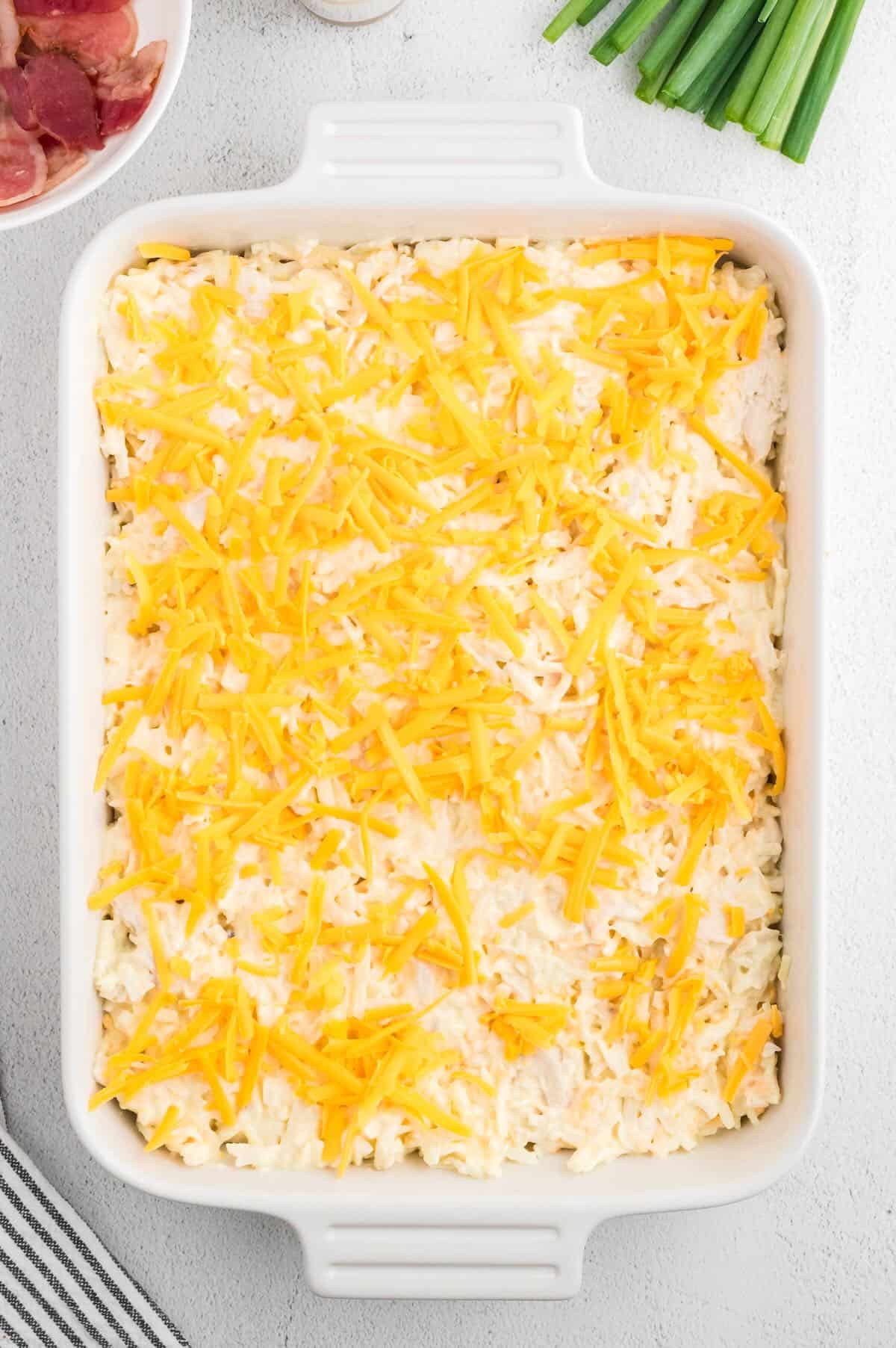 A baking dish full of hash brown chicken casserole topped with shredded cheese. 