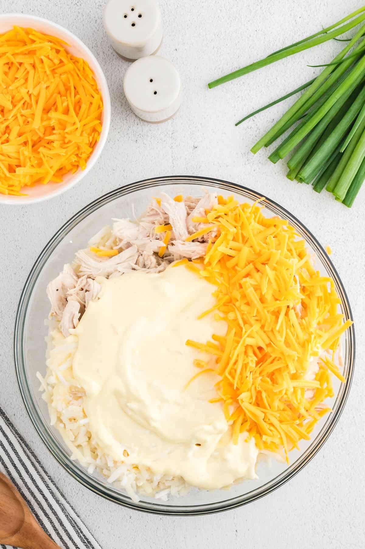 Hashbrowns and chicken in a mixing bowl with shredded cheese. 
