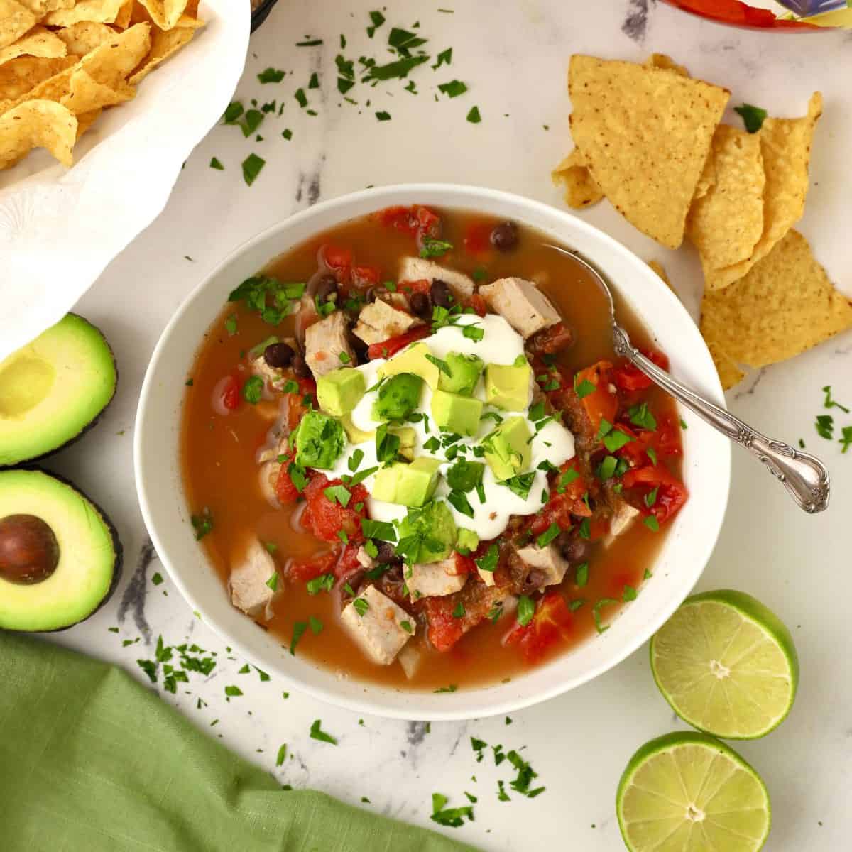 Mexican Pork Stew in a white bowl garnished with sour cream and avocado.