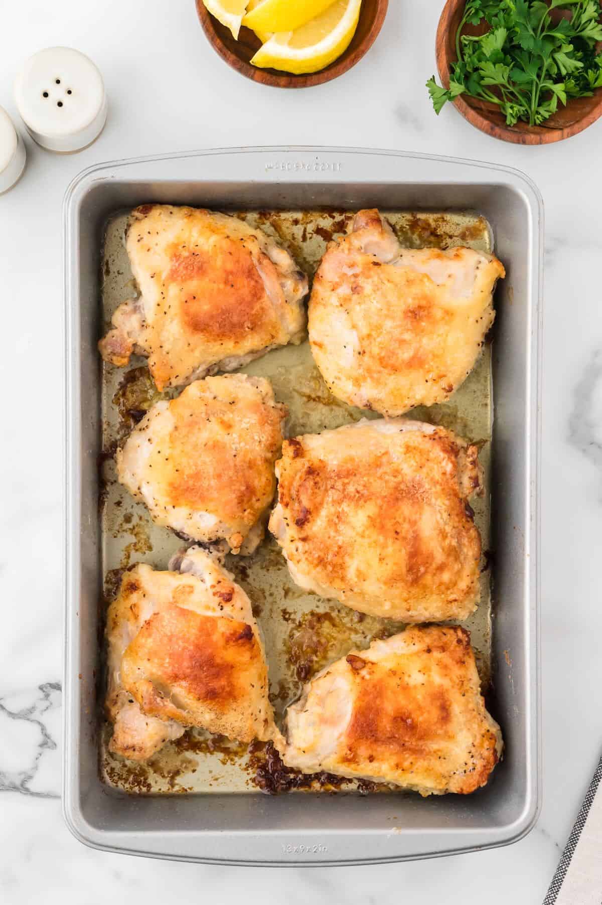 Chicken thighs with golden brown crispy skin in a baking pan.