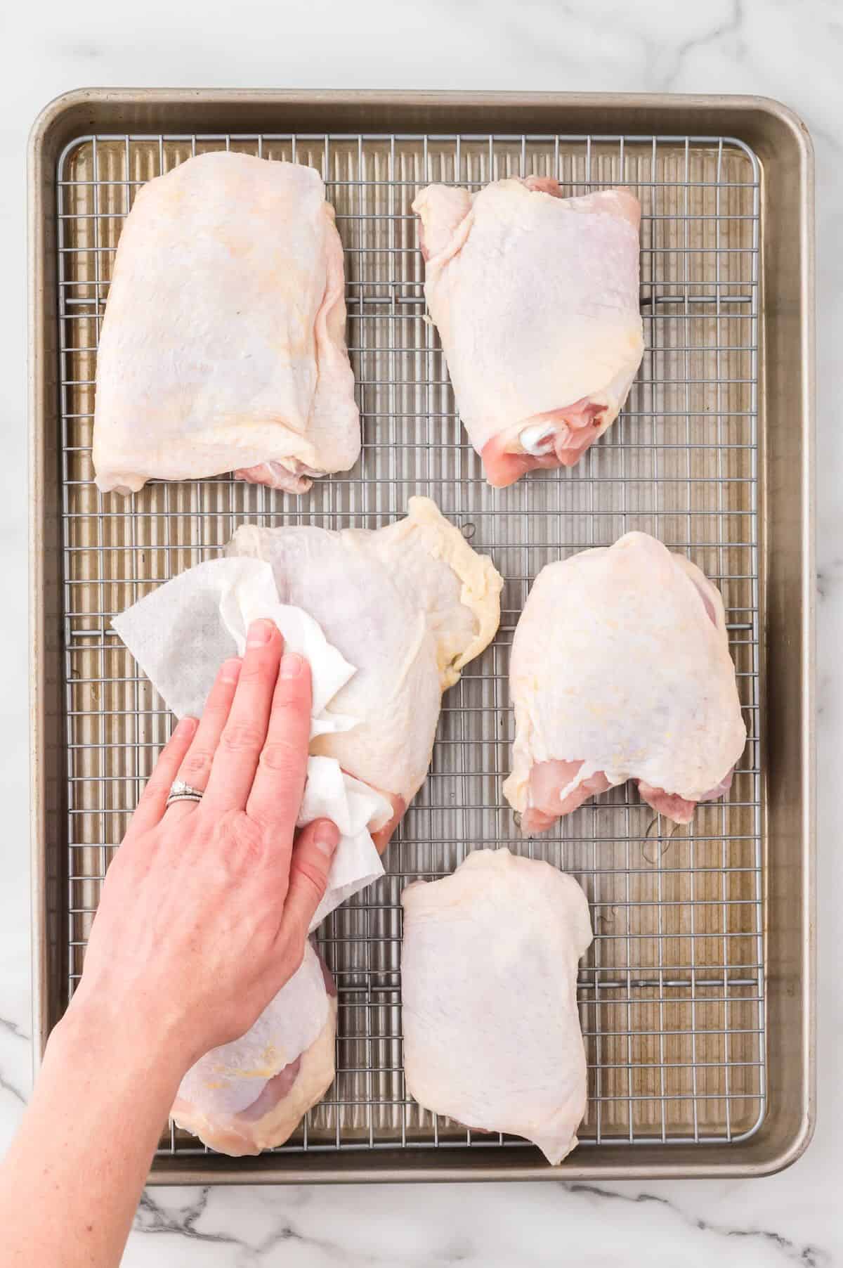 Using paper towels to pat chicken thighs dry. 