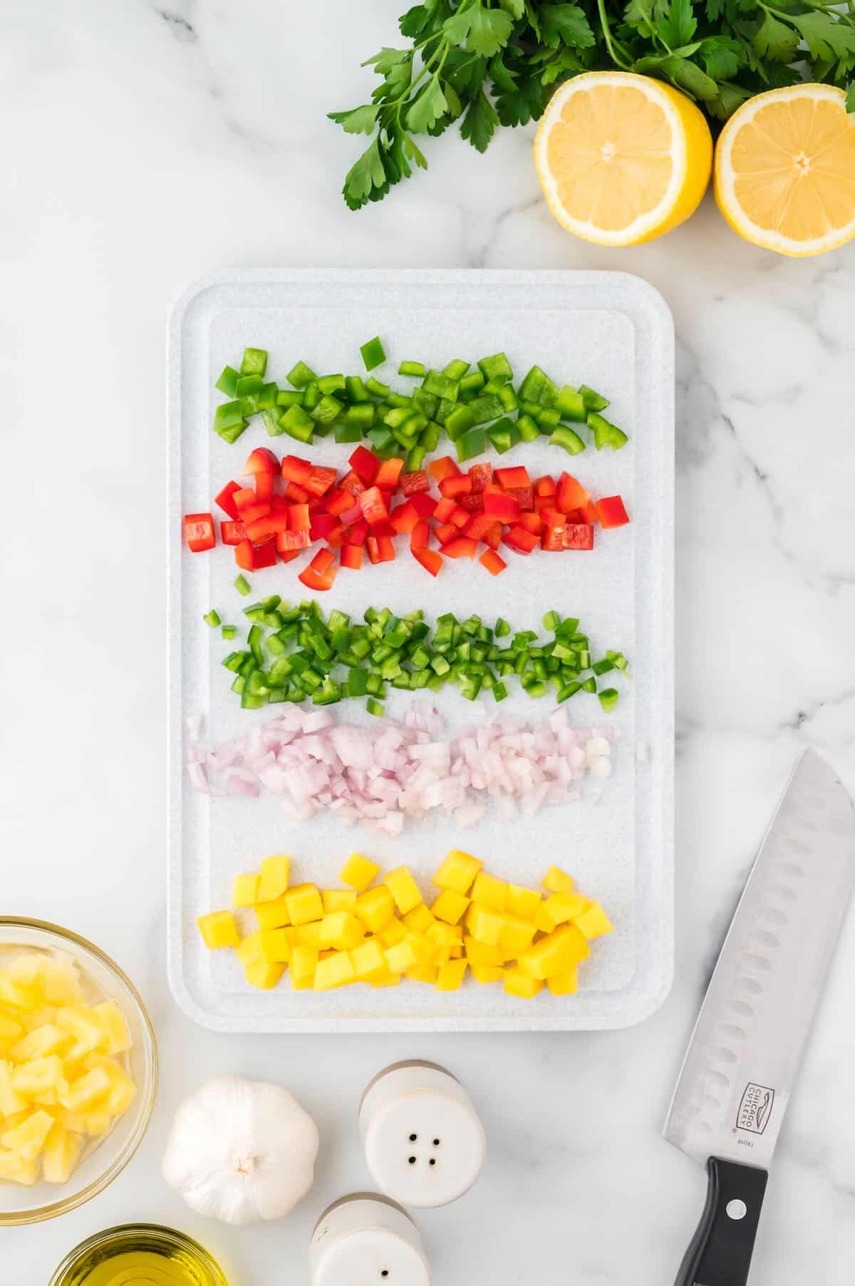 Chopped mango, bell pepper, jalapeno and pineapple on a cutting board. 