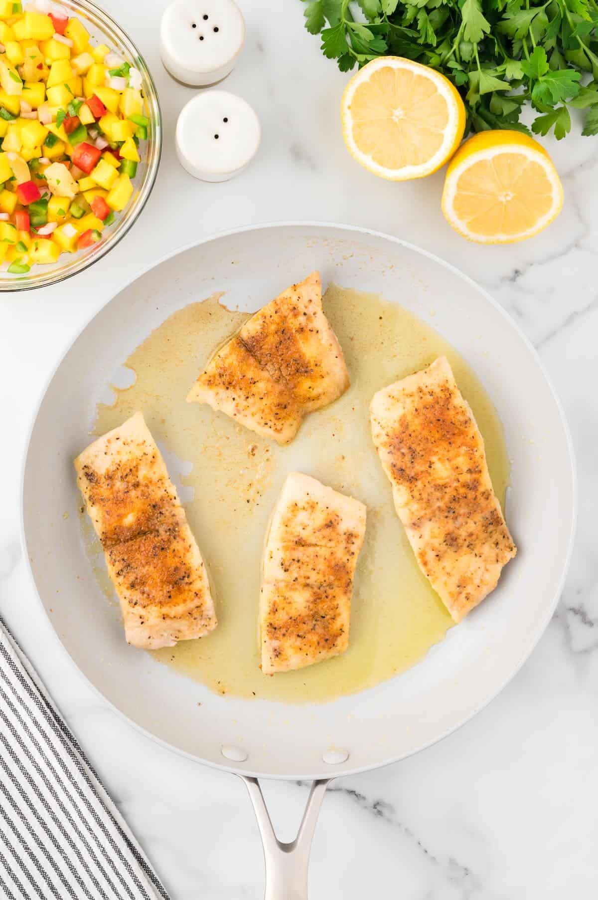 Four fish fillets in a white skillet cooking. 