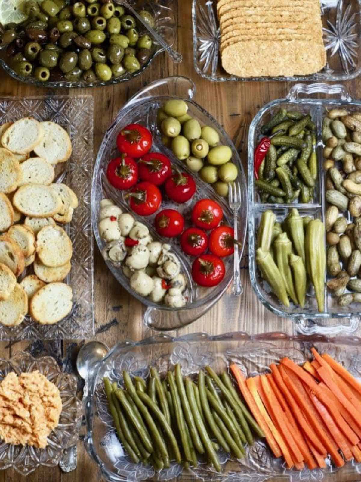 Several cut glass relish tray dishes full of pickles, vegetables and olives. 