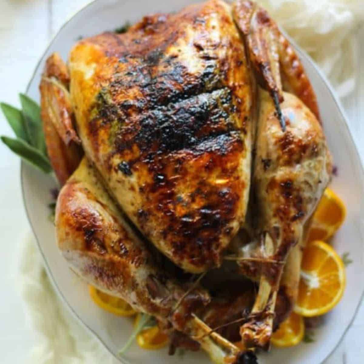 A whole roasted turkey on a platter garnished with sage leaves. 