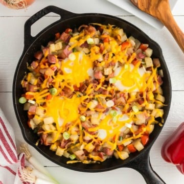 A cast-iron breakfast skillet topped with shredded cheese and four eggs.