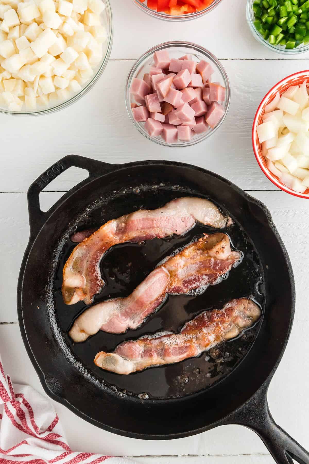 Three slices of bacon cooking in a cast iron skillet.