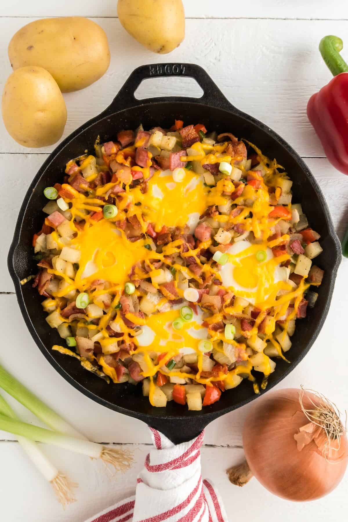 Cast iron breakfast full of potatoes, veggies, ham, bacon and eggs ready to serve. 