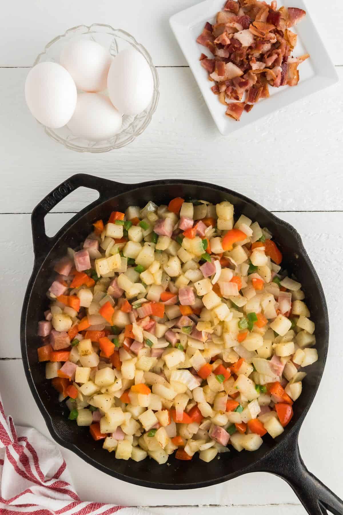 Cubed potatoes and other veggies cooking in a cast iron skillet.
