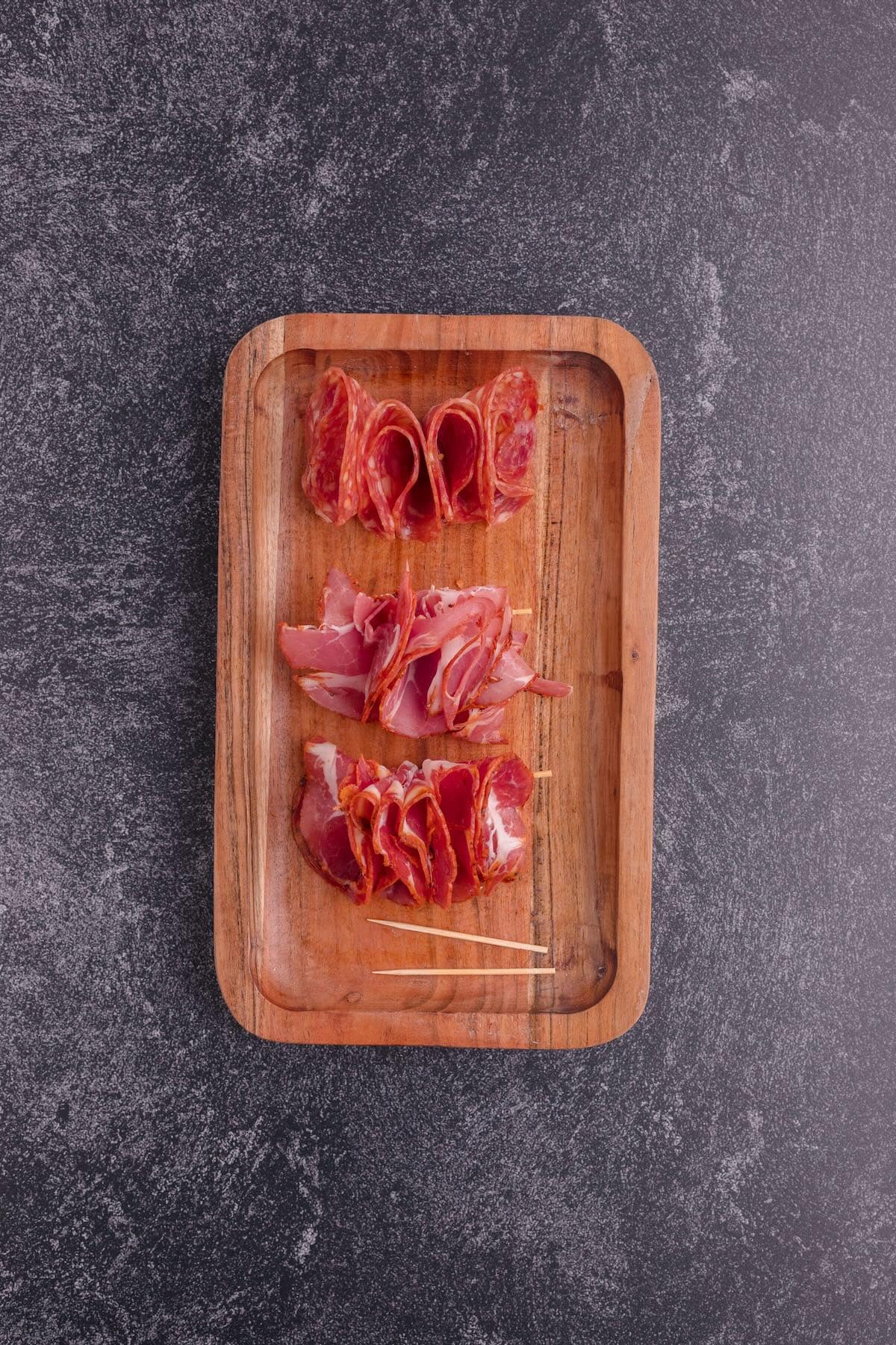 Folded cured meats for a charcuterie board with toothpicks holding them together. 