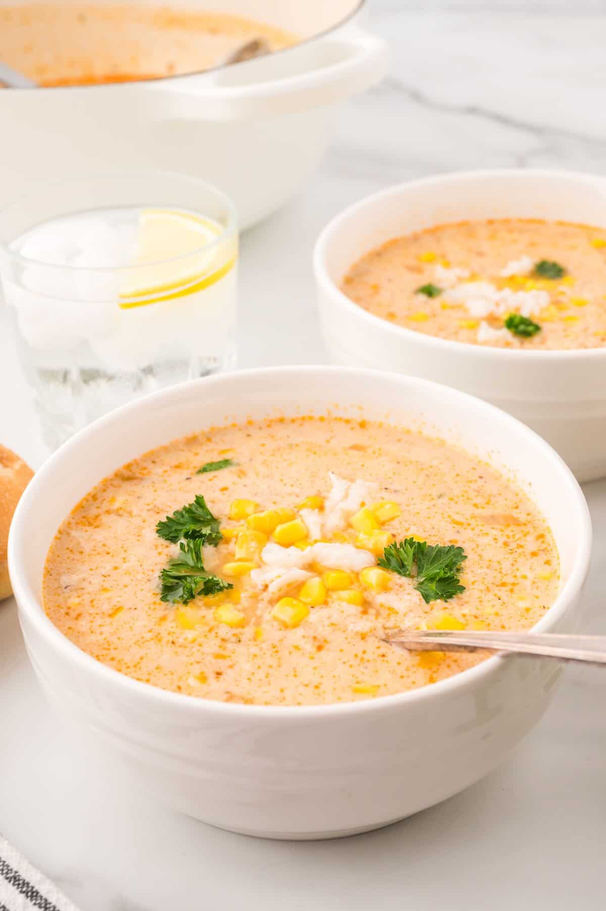 Two bowls of corn and crab bisque garnished with chopped parsley. 
