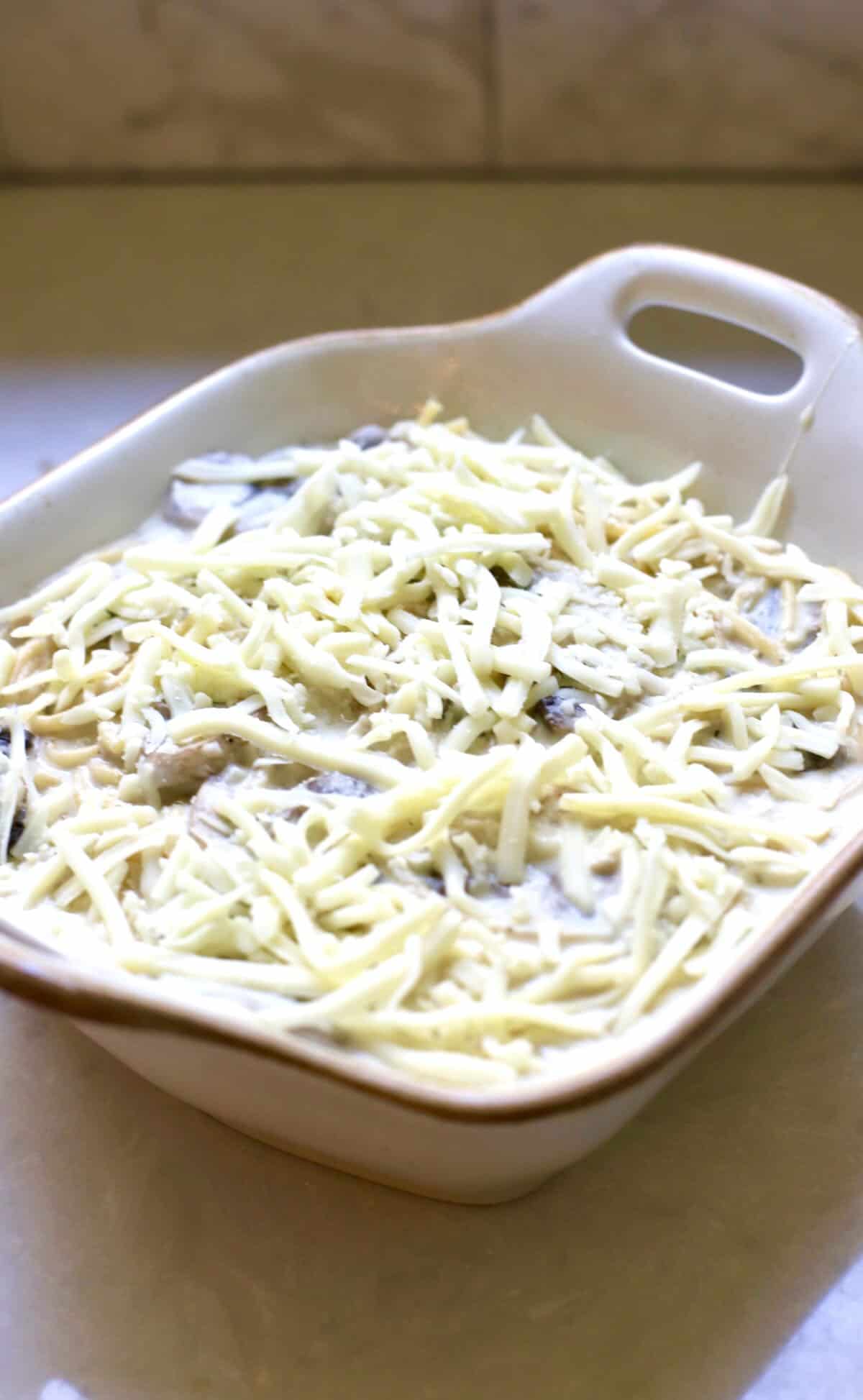 A baking dish with a turkey noodle casserole topped with shredded mozzarella cheese.