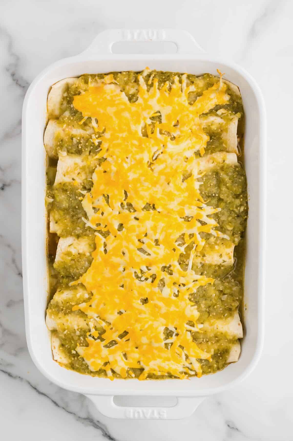 Baked green chicken enchiladas in a white baking dish topped with melted cheese. 
