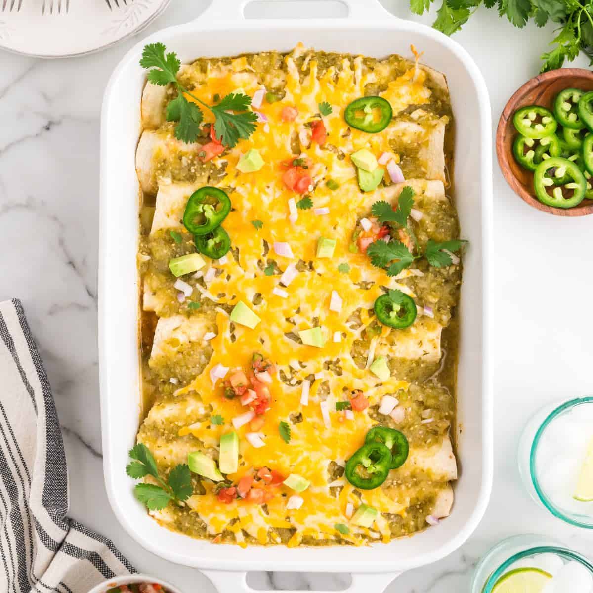 Green Chicken Enchiladas in a white baking dish topped with melted cheese and sliced jalapenos.