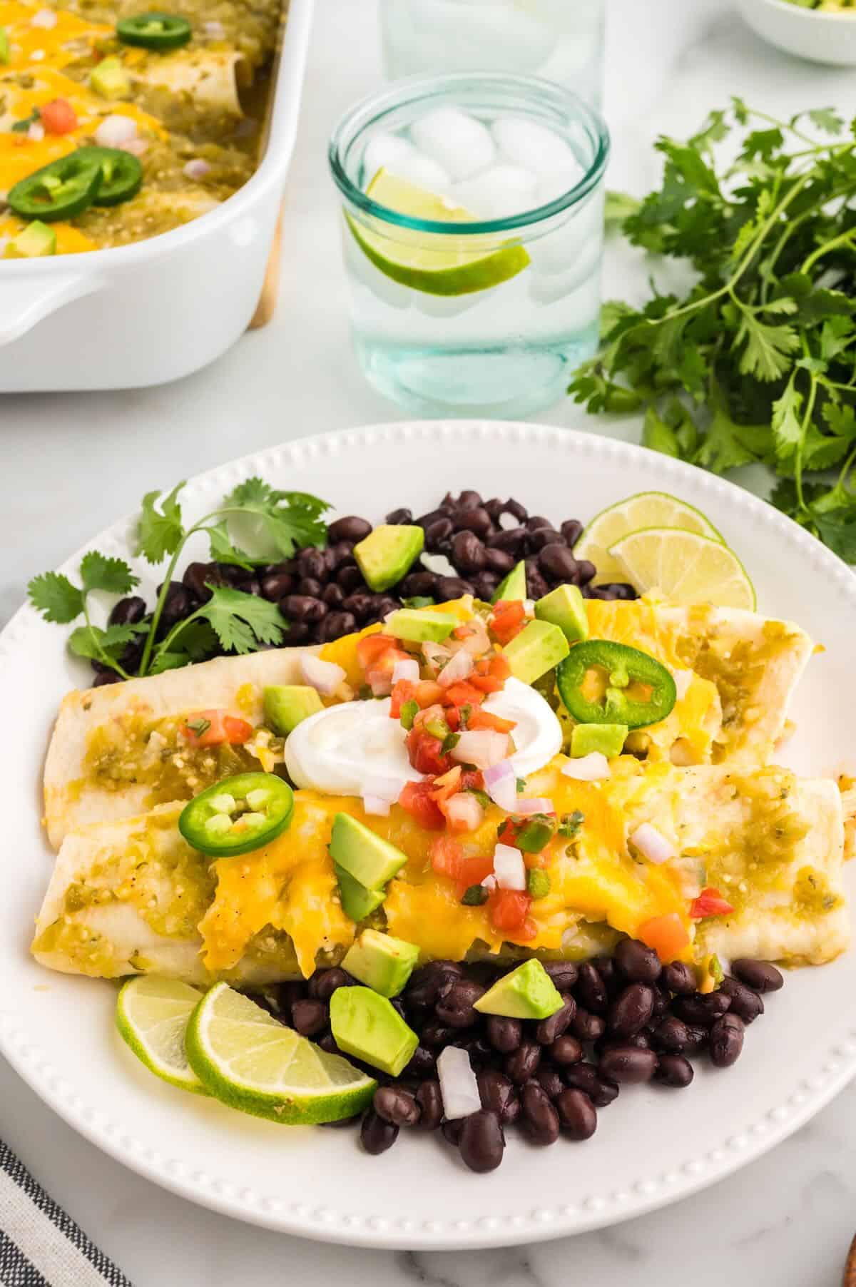 Green Chicken Enchiladas served over black beans on a white plate. 