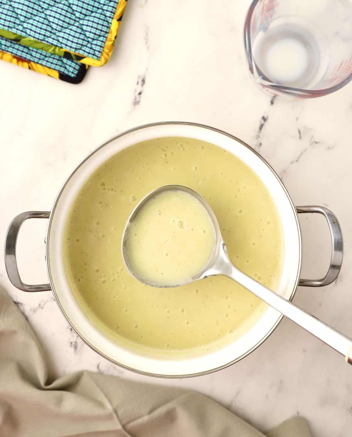 A soup ladle full of potato soup over a large pot of soup.