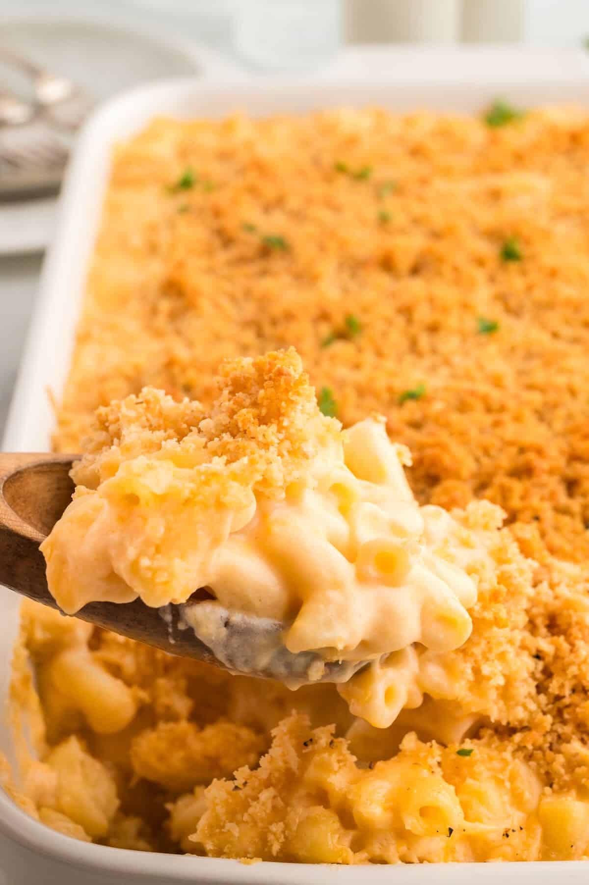 Southern Baked Mac and Cheese in a white baking dish with a wooden spoon digging in for a spoonful. 