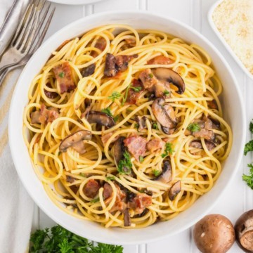 A bowl of mushroom carbonara topped with bacon and garnished with chopped parsley.