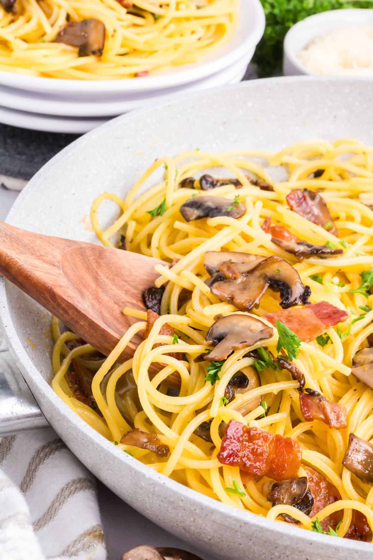 A bowl of cooked spaghetti with mushrooms and bacon.