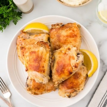 Oven-fried chicken thighs on a white plate garnished with lemon slices.