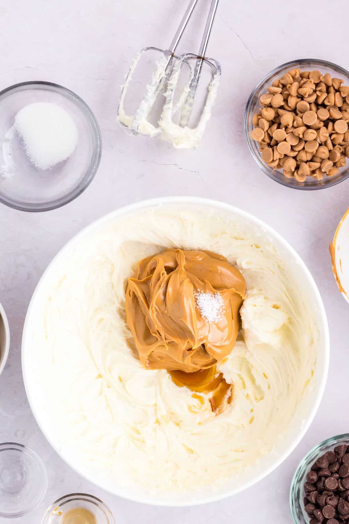 Adding peanut butter to a mixture of cream cheese and sugar in a white glass bowl 