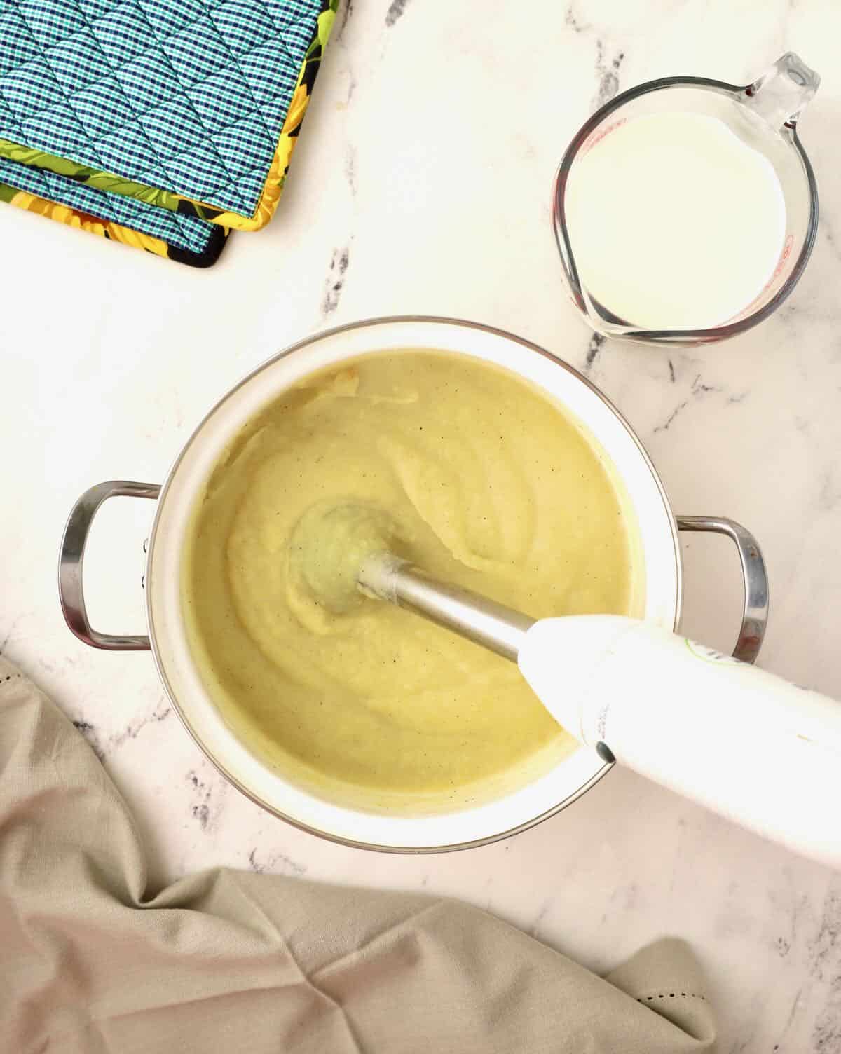 Using an immersion blender to puree cooked potatoes to make potato soup. 