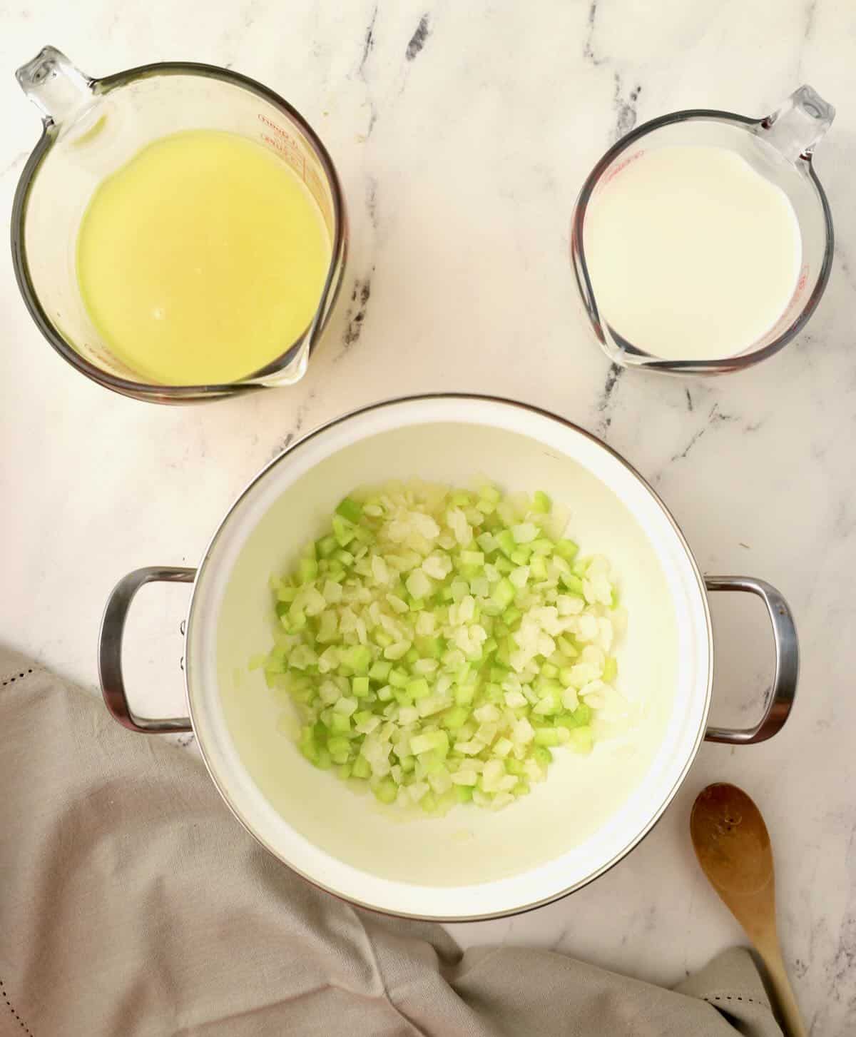 A soup pot with chopped celery and onions cooking in it. 