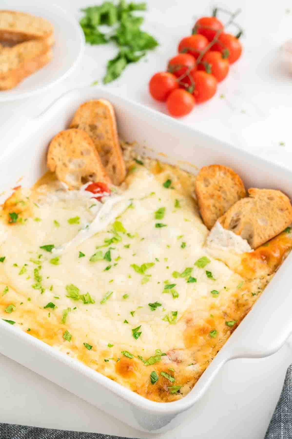 Baked ricotta dip in a white baking dish with crostini on the side.