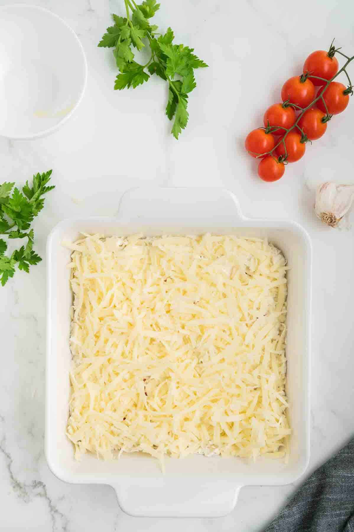 A square baking dish full of dip topped with shredded mozzarella cheese. 