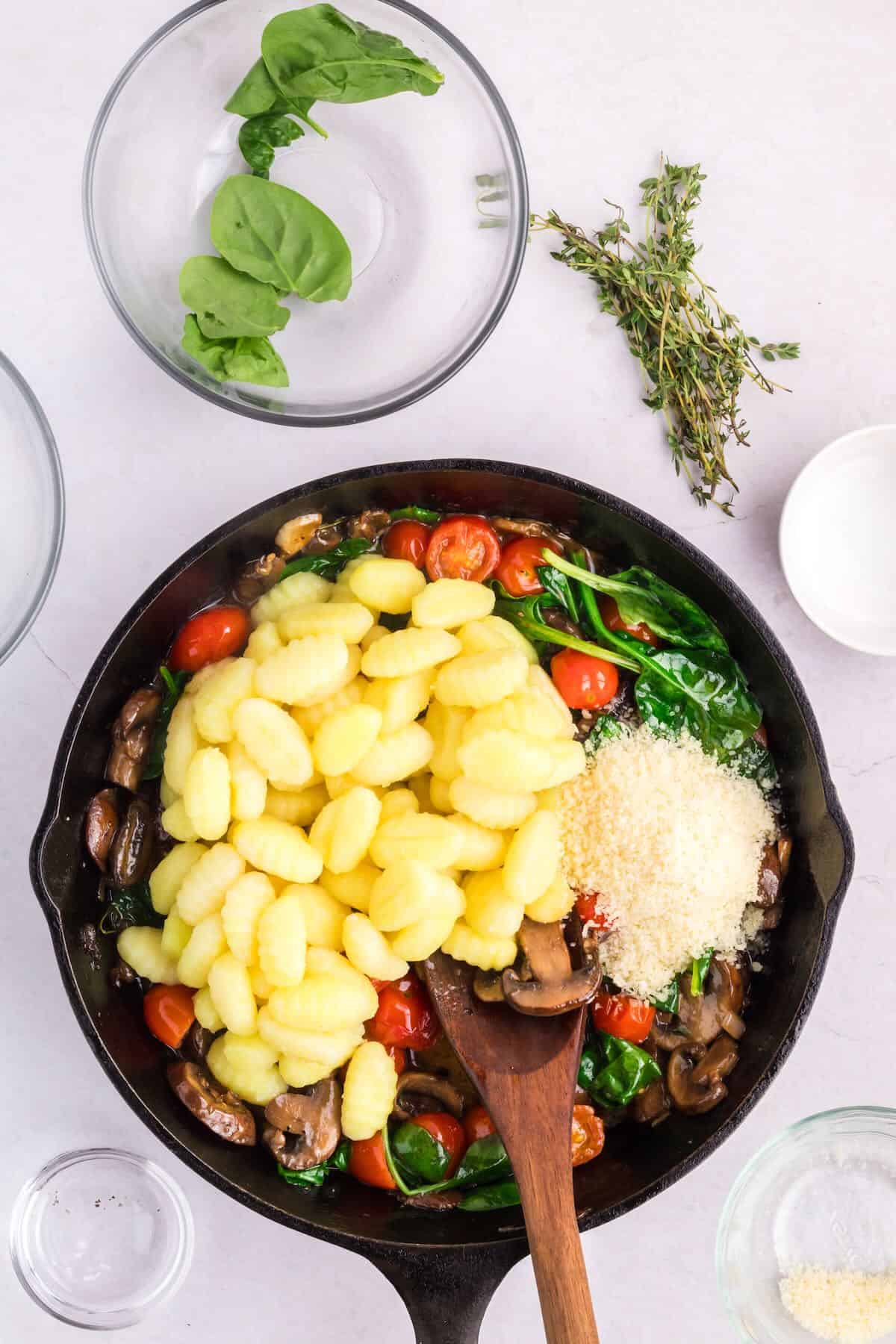 Cooked gnocchi is added to a cast-iron skillet along with spinach and tomatoes.