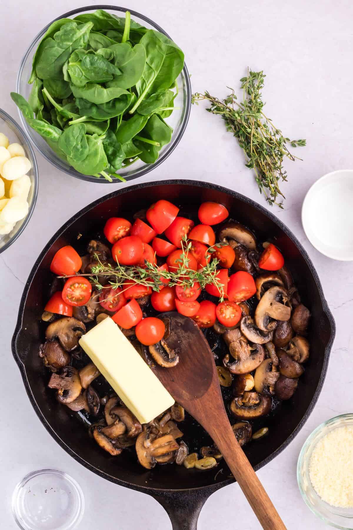 Sliced cherry tomatoes and a stick of butter in a skillet, along with sliced mushrooms. 