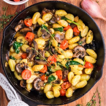 Skillet Gnocchi in a cast-iron skillet full of gnocchi, mushrooms, spinach, and cherry tomatoes.