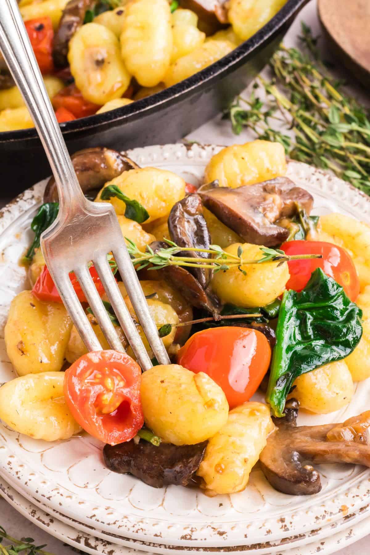 A serving of skillet gnocchi on a white plate with mushrooms, tomatoes, and spinach. 