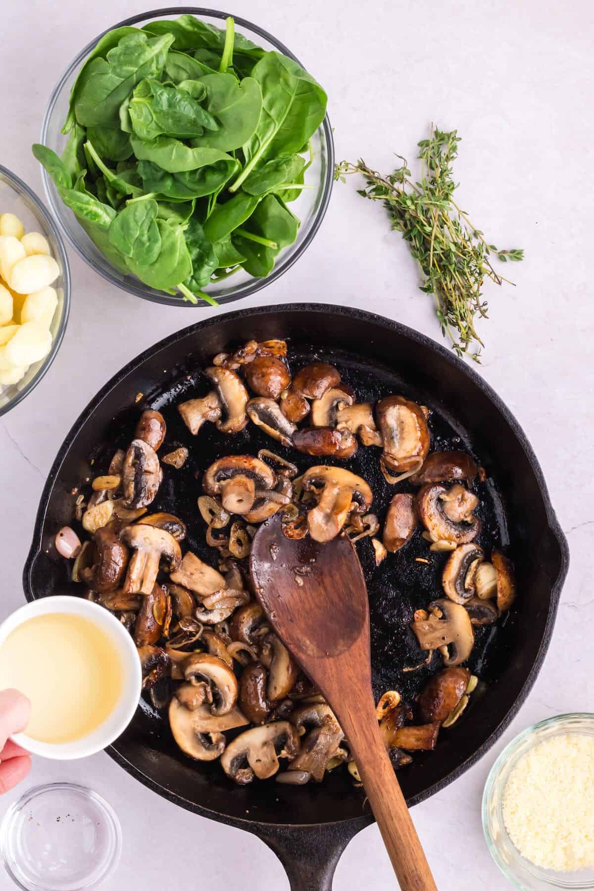 Sliced mushroom in a skillet with a cup of white wine being added. 