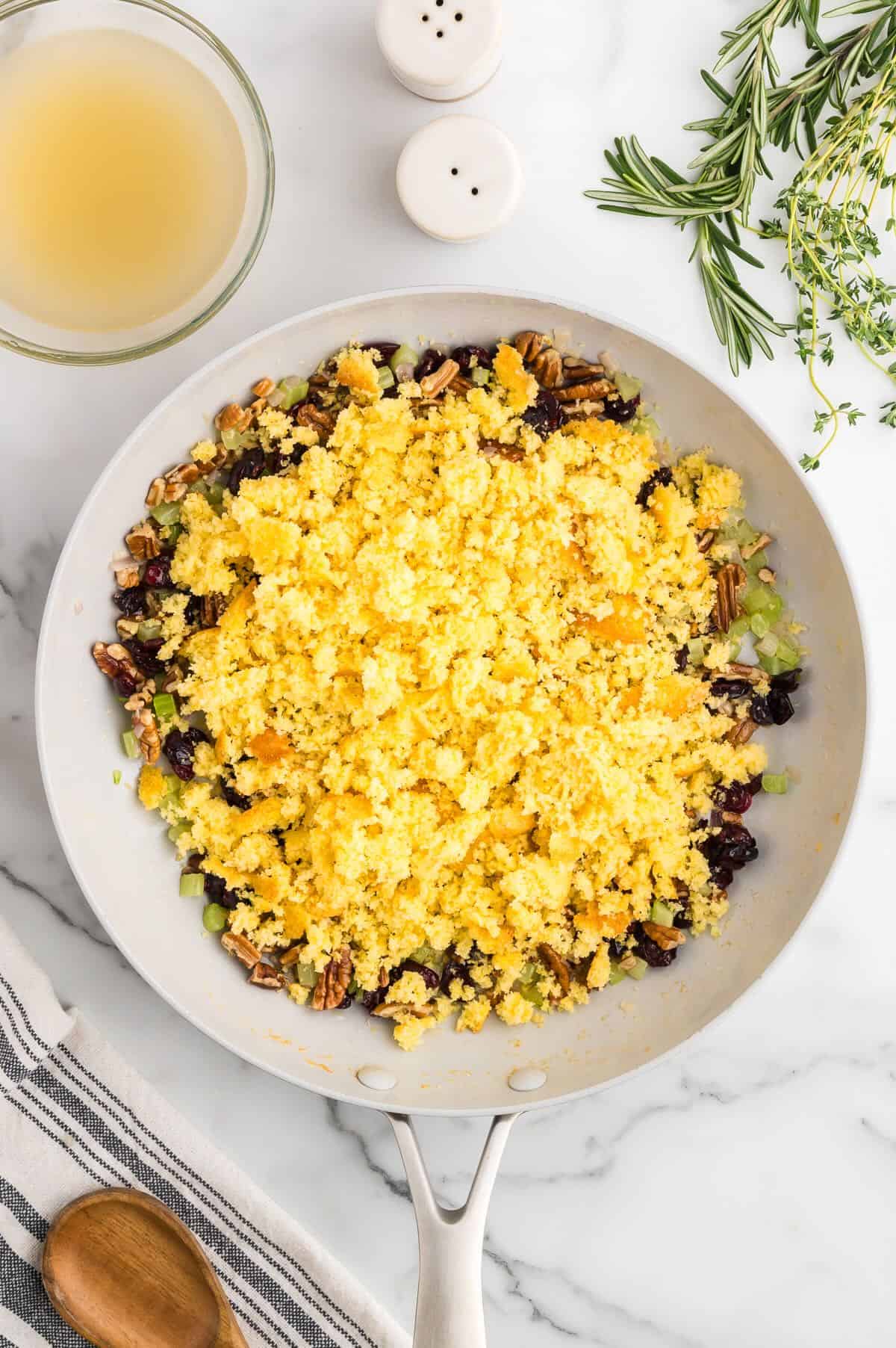 Crumbled cornbread over cooked veggies, dried cranberries, and pecans in a skillet. 