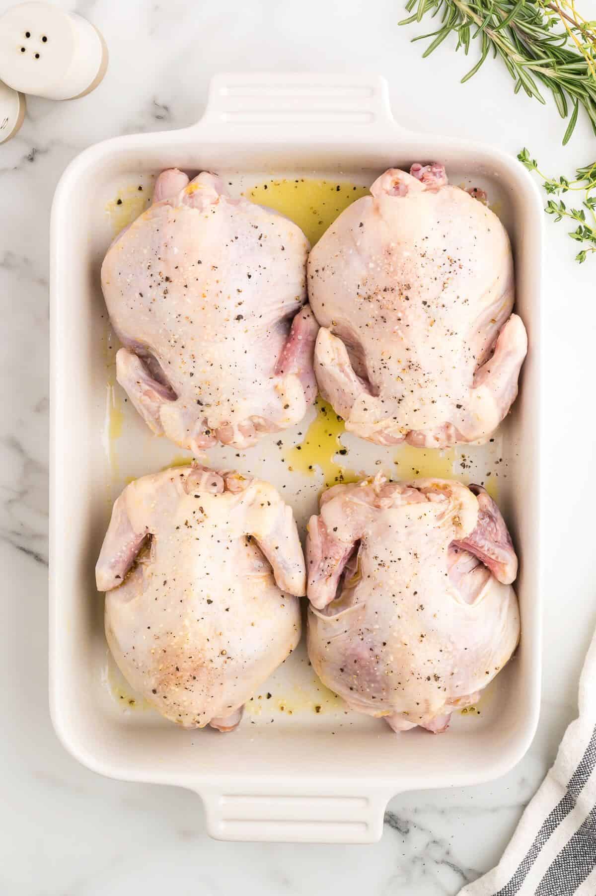 Four cornish game hens in a baking dish seasoned with salt and pepper.