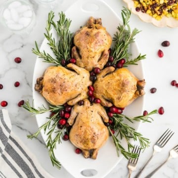 Stuffed Cornish Hens on a white platter garnished with sprigs of rosemary and fresh cranberries.
